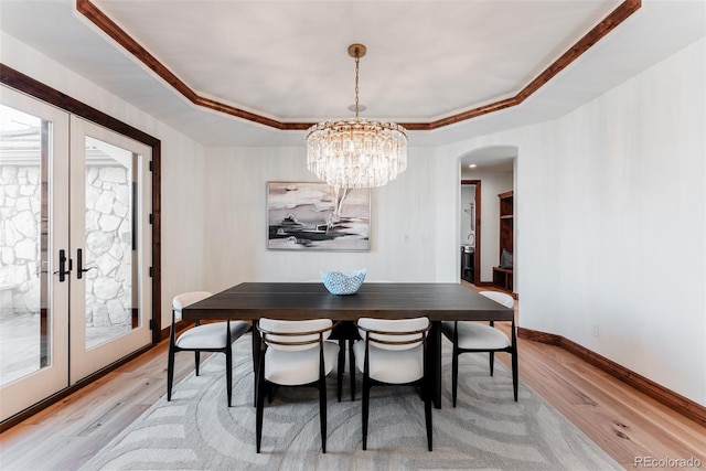 dining room featuring a notable chandelier, french doors, a tray ceiling, and light hardwood / wood-style flooring