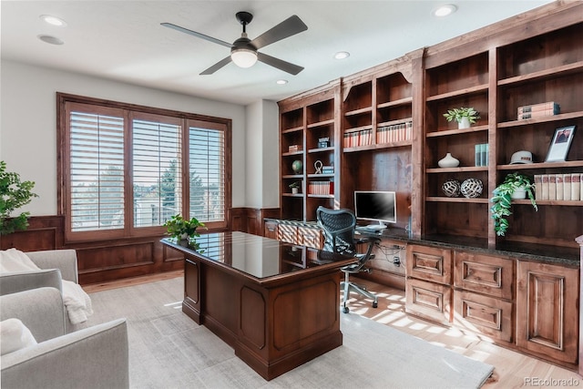 home office with light hardwood / wood-style flooring, ceiling fan, and wood walls