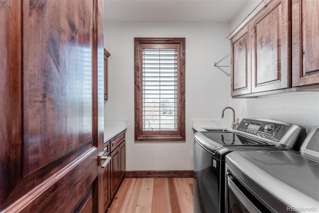 clothes washing area with cabinets, independent washer and dryer, light hardwood / wood-style floors, and sink