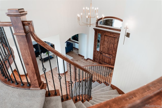 stairs with hardwood / wood-style floors, a towering ceiling, and a notable chandelier