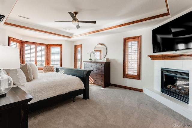 carpeted bedroom with ceiling fan, a tiled fireplace, and a tray ceiling