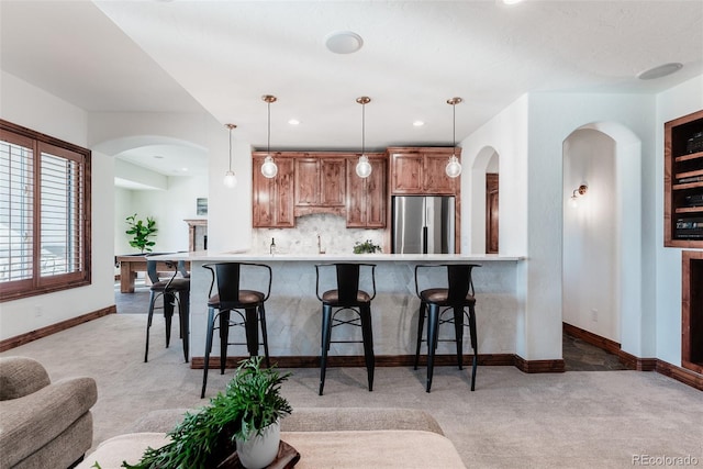 kitchen featuring kitchen peninsula, stainless steel refrigerator, pendant lighting, and light colored carpet