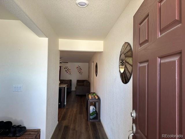 hall featuring a textured ceiling, dark wood-type flooring, and a textured wall