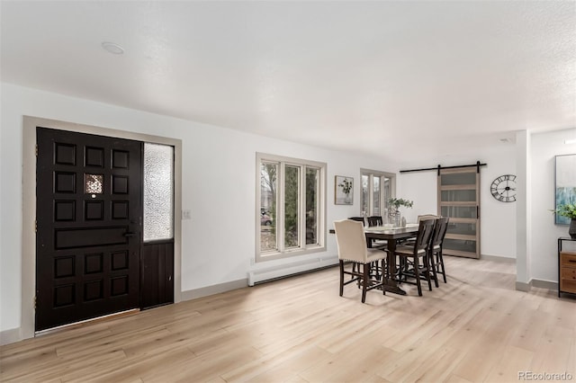 dining space with baseboard heating, a barn door, and light hardwood / wood-style flooring