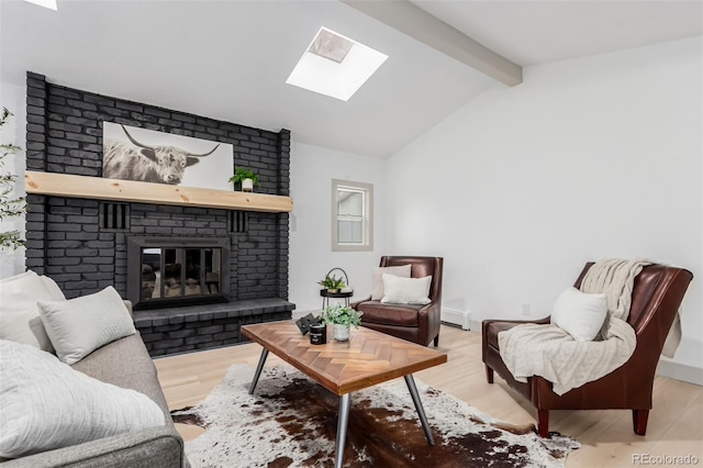 living room featuring baseboard heating, vaulted ceiling with skylight, a brick fireplace, and light wood-type flooring