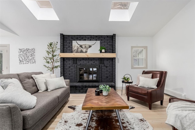 living room featuring lofted ceiling with skylight, a brick fireplace, and light hardwood / wood-style floors