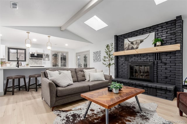 living room with a brick fireplace, vaulted ceiling with skylight, and light hardwood / wood-style floors