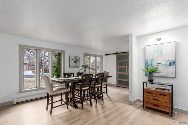 dining space with light wood-type flooring, a textured ceiling, a wealth of natural light, and a barn door