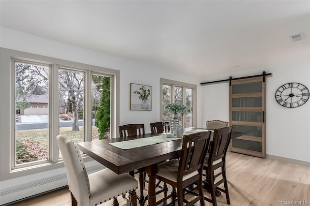 dining area featuring baseboard heating, a barn door, light hardwood / wood-style flooring, and a healthy amount of sunlight