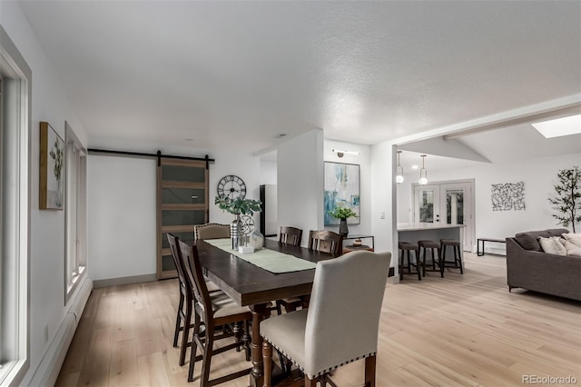 dining area featuring a baseboard heating unit, lofted ceiling, light hardwood / wood-style flooring, and a barn door