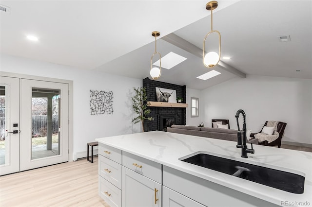 kitchen with sink, white cabinetry, pendant lighting, vaulted ceiling with skylight, and light stone countertops