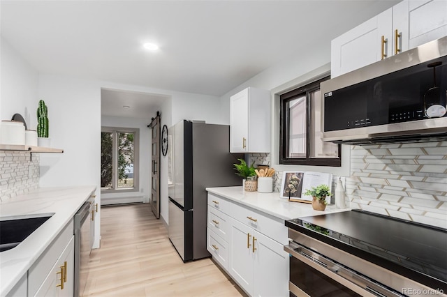 kitchen with light wood-type flooring, appliances with stainless steel finishes, white cabinetry, and backsplash