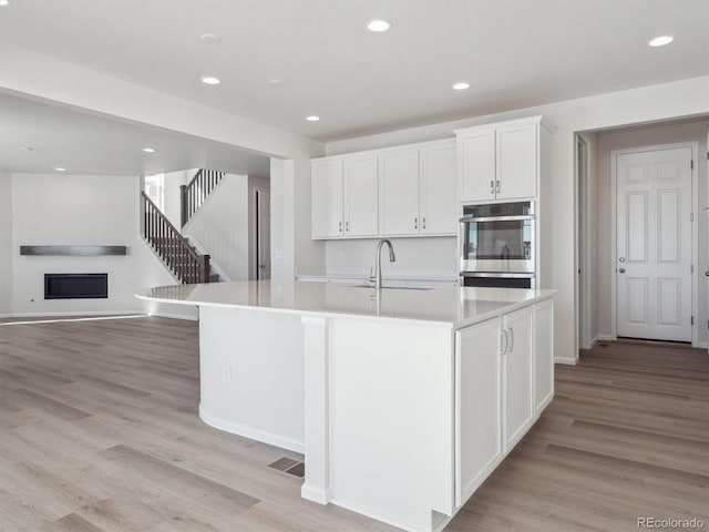 kitchen featuring white cabinets, light hardwood / wood-style floors, sink, and an island with sink