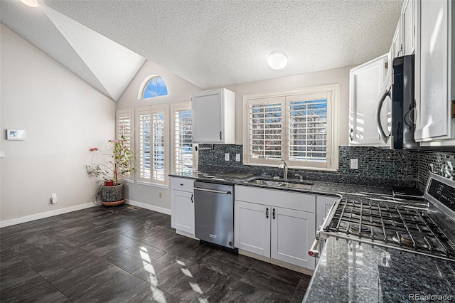 kitchen featuring sink, appliances with stainless steel finishes, white cabinetry, dark stone countertops, and vaulted ceiling