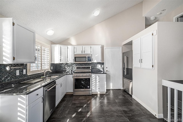 kitchen with appliances with stainless steel finishes, white cabinetry, sink, dark stone countertops, and backsplash