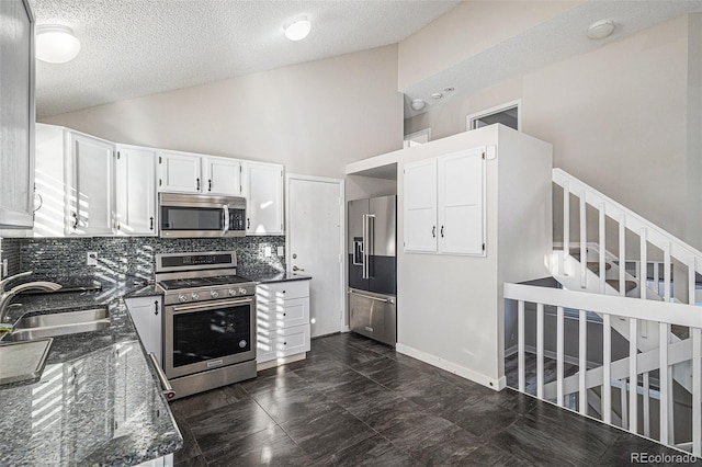 kitchen with sink, white cabinetry, high vaulted ceiling, appliances with stainless steel finishes, and dark stone counters