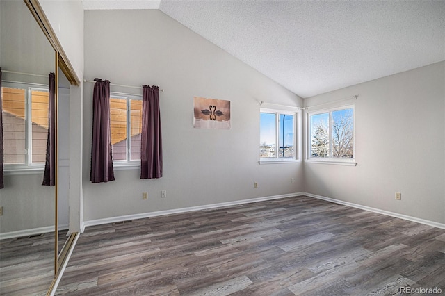 empty room featuring lofted ceiling, dark hardwood / wood-style floors, and a textured ceiling