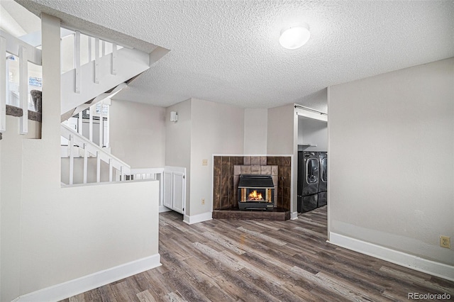 unfurnished living room with hardwood / wood-style flooring, a tile fireplace, washer and dryer, and a textured ceiling