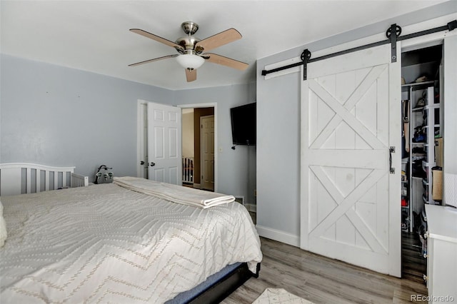 bedroom featuring a closet, a barn door, ceiling fan, and light hardwood / wood-style flooring