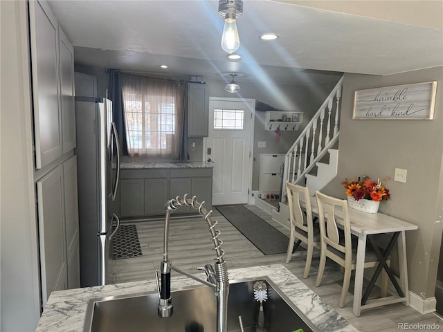 kitchen with gray cabinets, decorative backsplash, stainless steel fridge, and light stone counters