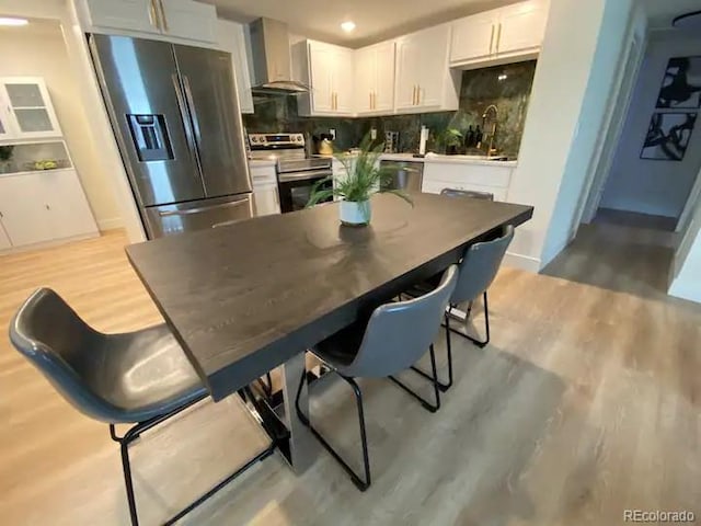 kitchen with decorative backsplash, wall chimney exhaust hood, stainless steel appliances, white cabinets, and light hardwood / wood-style floors