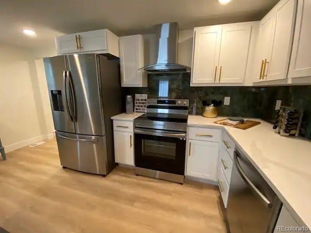 kitchen with stainless steel appliances, wall chimney exhaust hood, white cabinets, decorative backsplash, and light hardwood / wood-style flooring