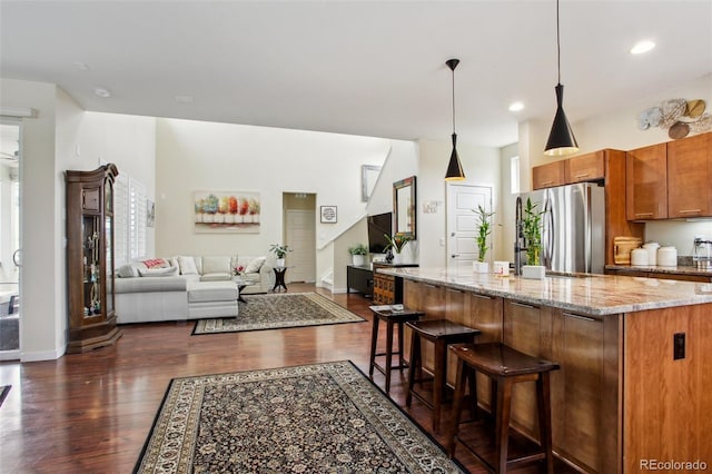 kitchen with dark hardwood / wood-style floors, pendant lighting, stainless steel refrigerator, a kitchen breakfast bar, and light stone countertops