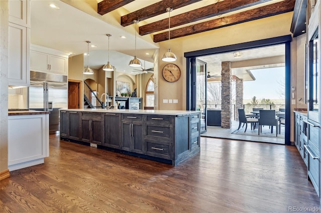 kitchen featuring built in fridge, white cabinetry, pendant lighting, and a kitchen island with sink