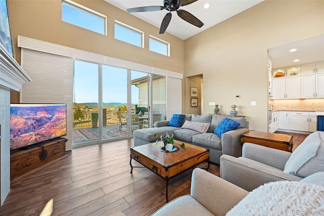 living room featuring ceiling fan, a towering ceiling, wood finished floors, and a wealth of natural light