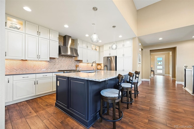 kitchen with backsplash, white cabinetry, a sink, wall chimney range hood, and high end refrigerator