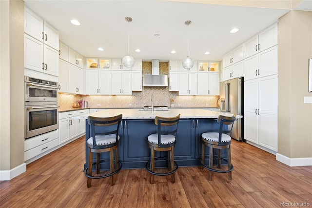 kitchen featuring light countertops, wall chimney exhaust hood, white cabinetry, and stainless steel appliances