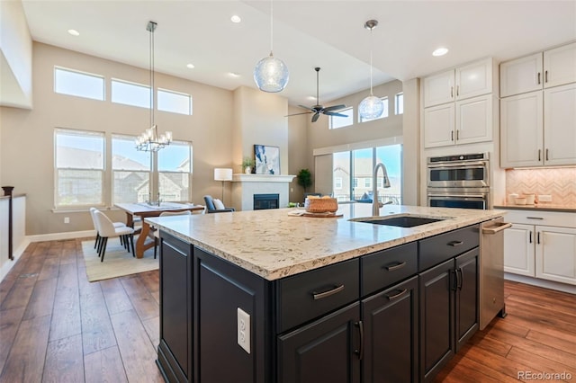 kitchen with a sink, a fireplace, wood-type flooring, ceiling fan with notable chandelier, and white cabinetry