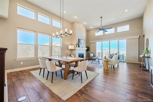 dining space featuring a high ceiling, a glass covered fireplace, plenty of natural light, and ceiling fan with notable chandelier