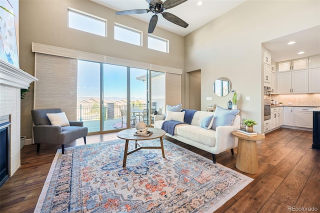 living area with ceiling fan, dark wood finished floors, a glass covered fireplace, and a high ceiling