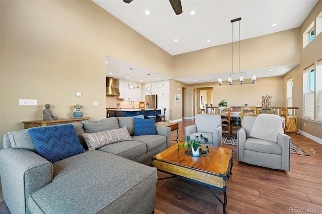 living area featuring a towering ceiling, wood finished floors, baseboards, ceiling fan, and plenty of natural light