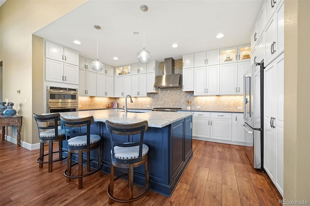 kitchen with wall chimney range hood, white cabinets, a sink, appliances with stainless steel finishes, and backsplash