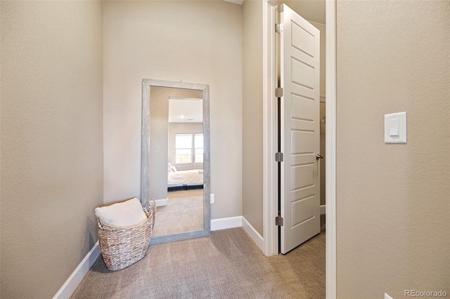 hallway featuring baseboards, light colored carpet, and a textured wall