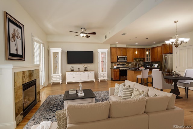 living room featuring dark wood-type flooring, ceiling fan with notable chandelier, and a tile fireplace