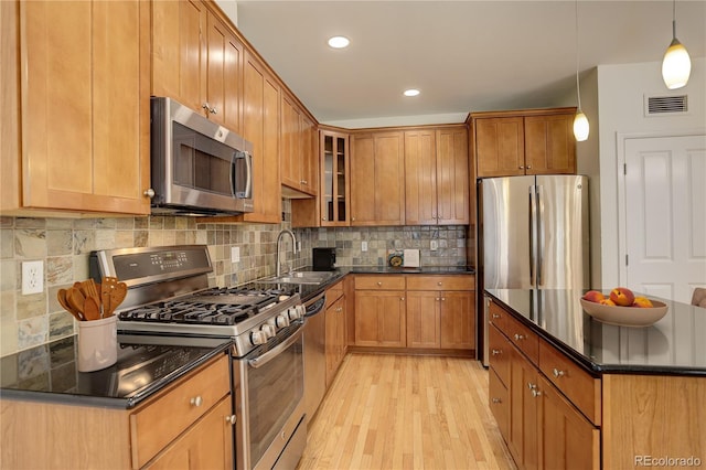 kitchen with appliances with stainless steel finishes, decorative light fixtures, sink, decorative backsplash, and light hardwood / wood-style flooring