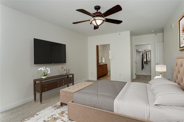 bedroom with ensuite bathroom, a spacious closet, light colored carpet, and ceiling fan