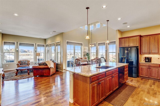 kitchen with a wealth of natural light, sink, black appliances, and a center island with sink