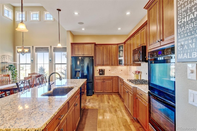 kitchen featuring light stone counters, black appliances, sink, light hardwood / wood-style flooring, and hanging light fixtures