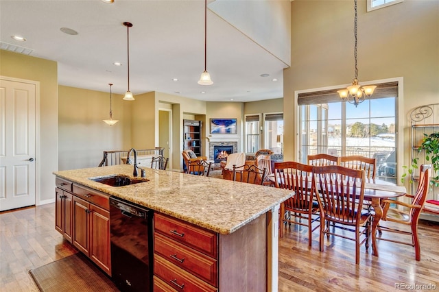 kitchen featuring light hardwood / wood-style flooring, an island with sink, hanging light fixtures, and black dishwasher