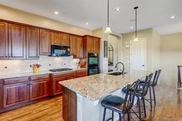 kitchen with black appliances, light hardwood / wood-style flooring, sink, and an island with sink