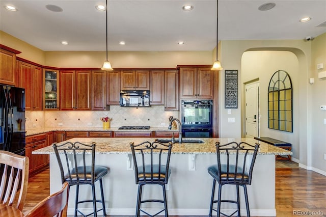 kitchen with dark hardwood / wood-style flooring, a kitchen island with sink, sink, black appliances, and pendant lighting