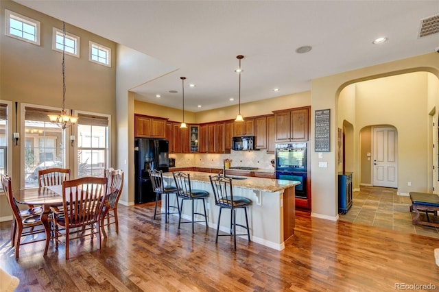 kitchen featuring black appliances, light stone counters, light wood-type flooring, and a breakfast bar area