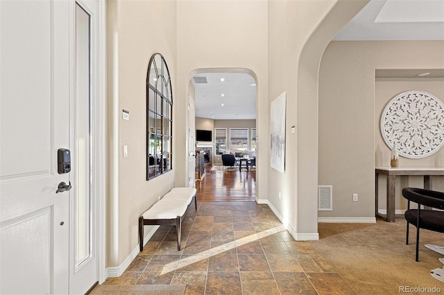 entryway with arched walkways, baseboards, visible vents, and stone tile floors