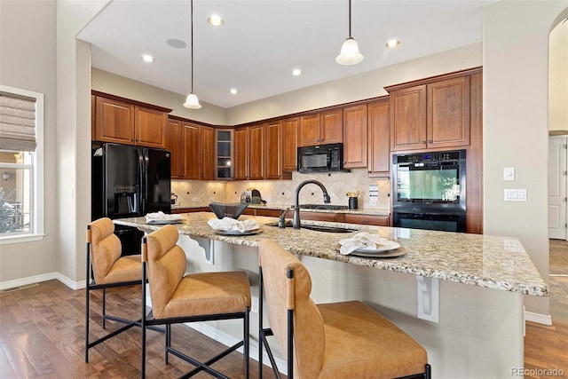 kitchen featuring light stone countertops, a sink, hanging light fixtures, brown cabinets, and black appliances