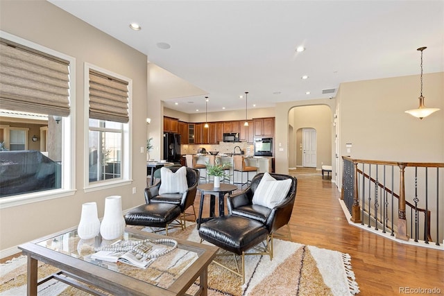 living room featuring arched walkways, recessed lighting, visible vents, baseboards, and light wood-type flooring