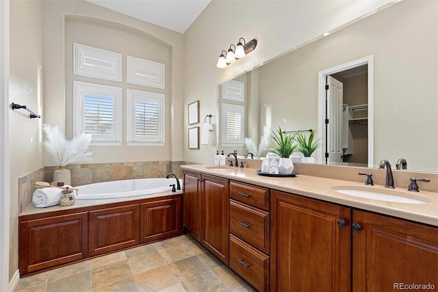 bathroom with double vanity, a spacious closet, a sink, and a bath